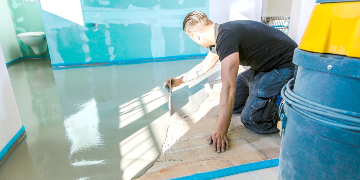 Ausgleichsmasse für Boden wird mit Glättkelle auf unebenem Untergrund verteilt