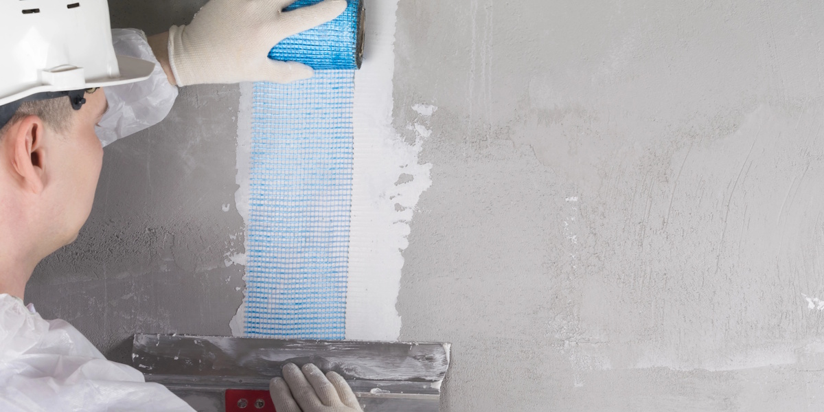 Handwerker bringt Armierungsgewebe und Putz auf eine Wand auf zur Reparatur von Rissen im Mauerwerk