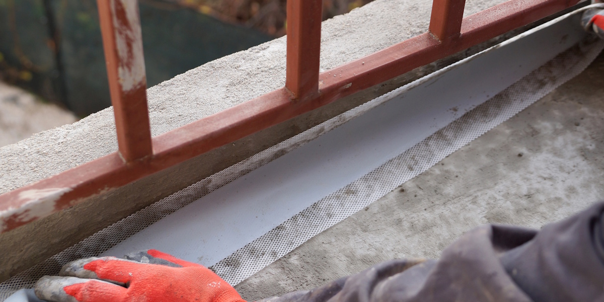 Abdichtungsarbeiten am Fuß einer Metallbrüstung auf Betonfläche mit Dichtband und Beschichtung im Anschlussbereich.