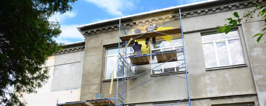 Handwerker sanieren eine Gebäudefassade auf einem Gerüst im Rahmen von Bautenschutzarbeiten