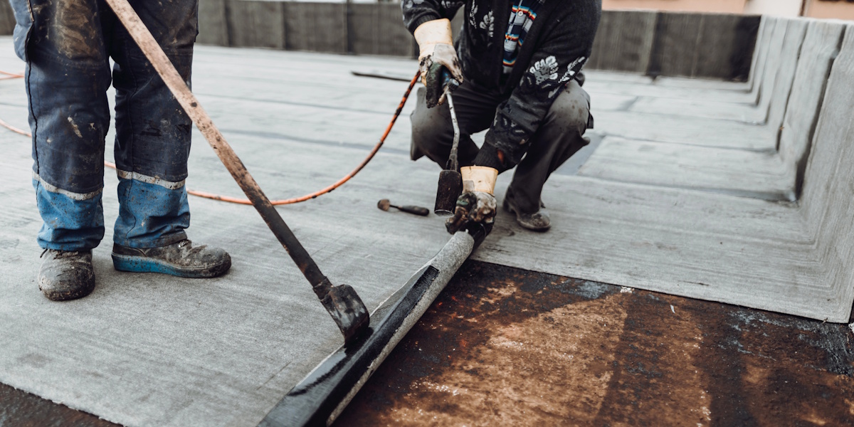 Terrasse Abdichtung_Terrasse abdichten Zwei Arbeiter verlegen mit Brenner eine bituminöse Schweißbahn auf einer Terrasse oder Flachdachfläche.
