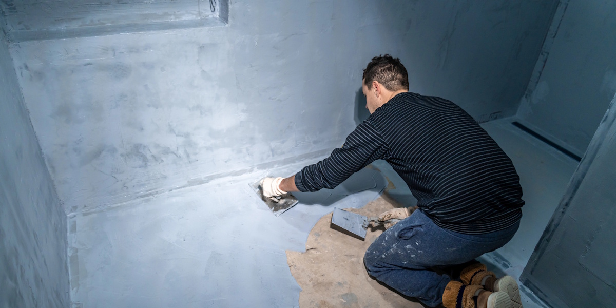 Handwerker glättet 2K-Dichtschlämme auf einer Kellerwand mit einer Kelle.