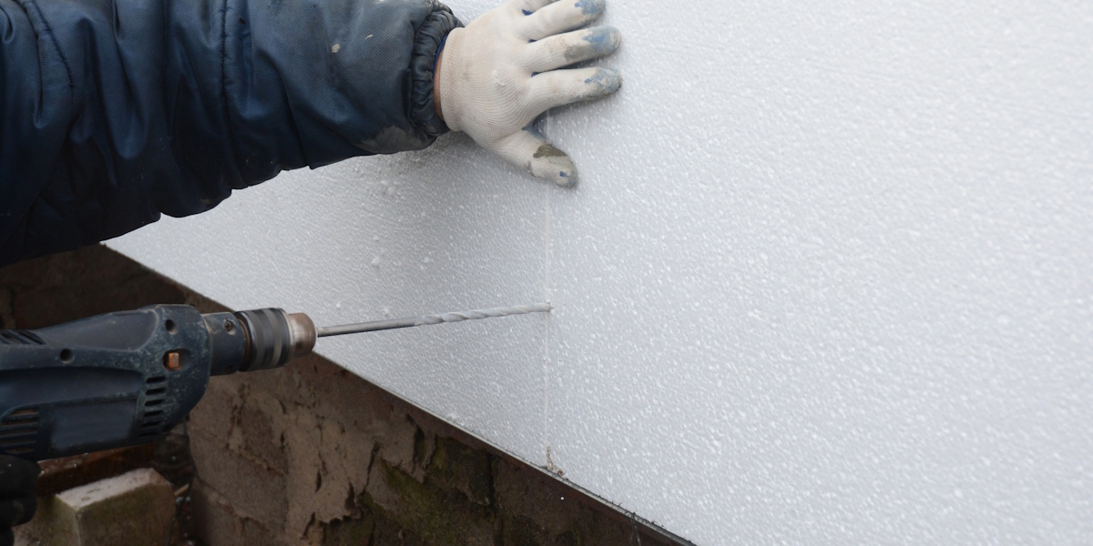 Außenwand gegen Feuchtigkeit schützen_Methoden Handwerker befestigt Dämmplatten an einer Außenwand, um die Fassade vor Feuchtigkeit zu schützen.