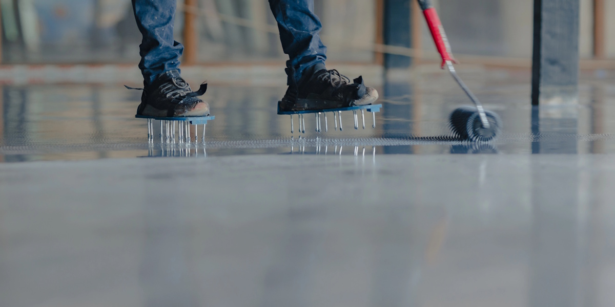 Handwerker trägt eine flüssige Bodenbeschichtung außen mit einer Stachelwalze auf.
