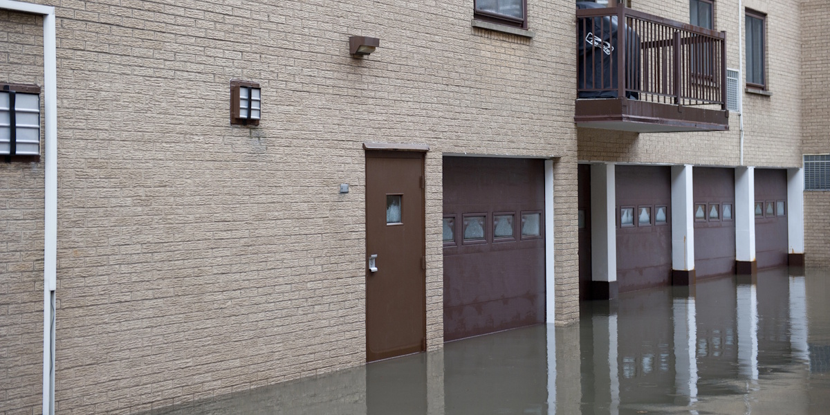 Überfluteter Außenwandbereich eines Gebäudes mit Wasser vor Garagentoren und Hauseingang.