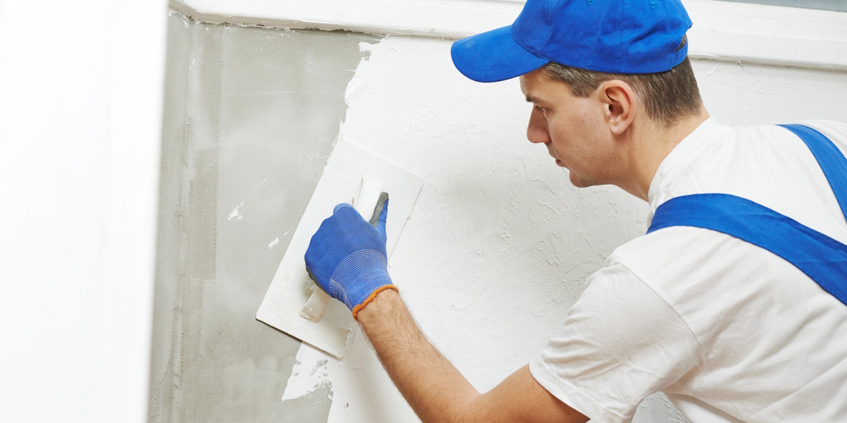 Handwerker trägt Putz auf eine sanierte Wand auf nach Einbau einer Feuchtigkeitssperre im Mauerwerk.