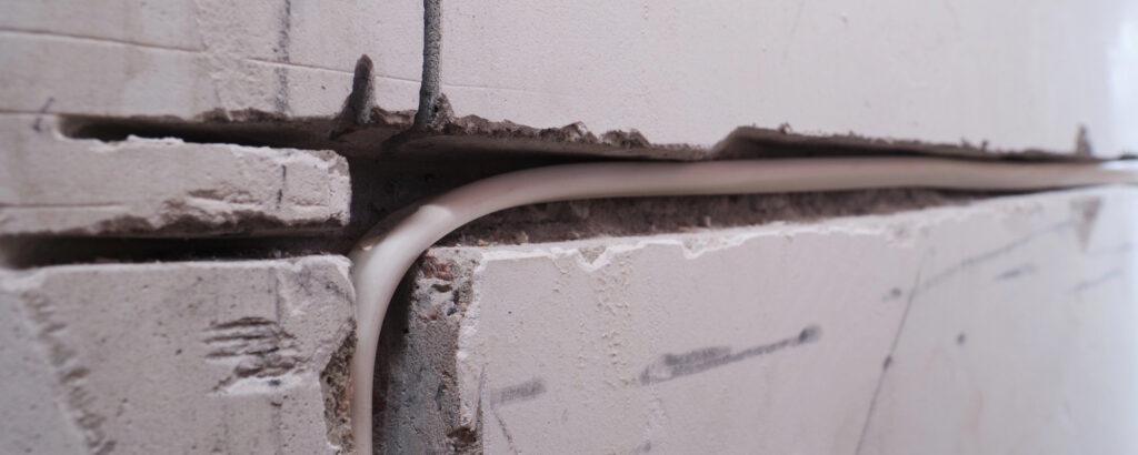 Kabel verläuft durch eine geöffnete Wandfuge als Beispiel für eine Wanddurchführung für Kabel.